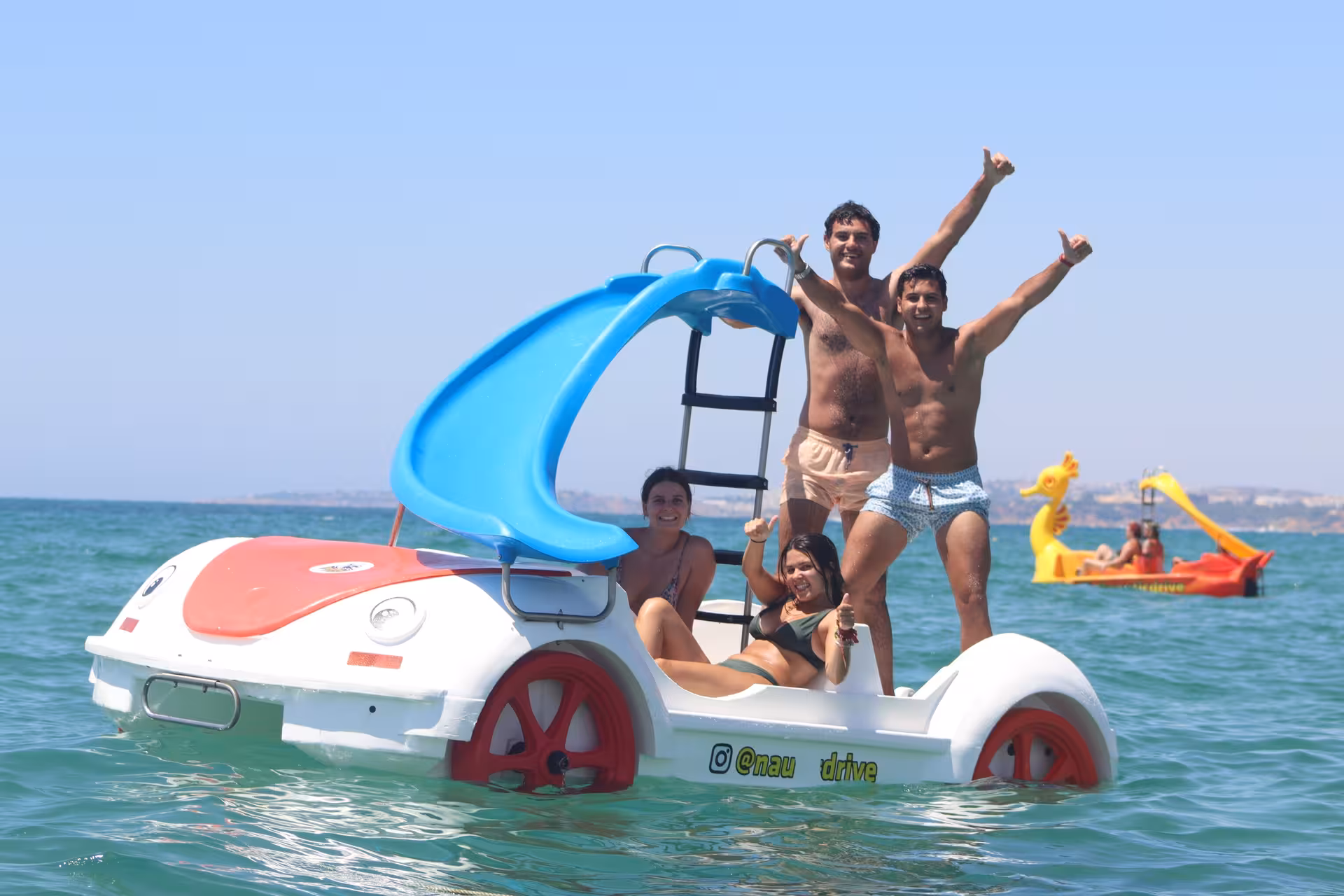 Group of friends having fun on a pedal boat with a blue water slide during a family-friendly sea tour.