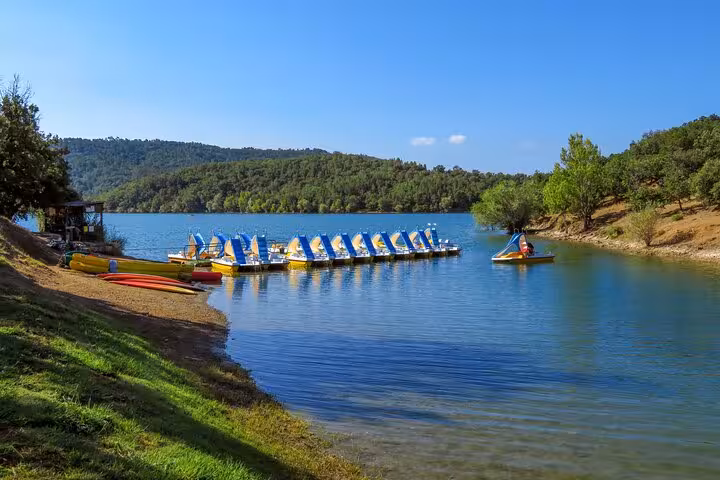 Colorful pedal boats docked on a calm lake surrounded by forested hills near Grasse, French Riviera