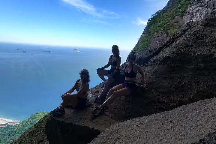 Three hikers enjoy a scenic ocean view from a cliff on the Pedra da Gávea Garganta do Céu trail.