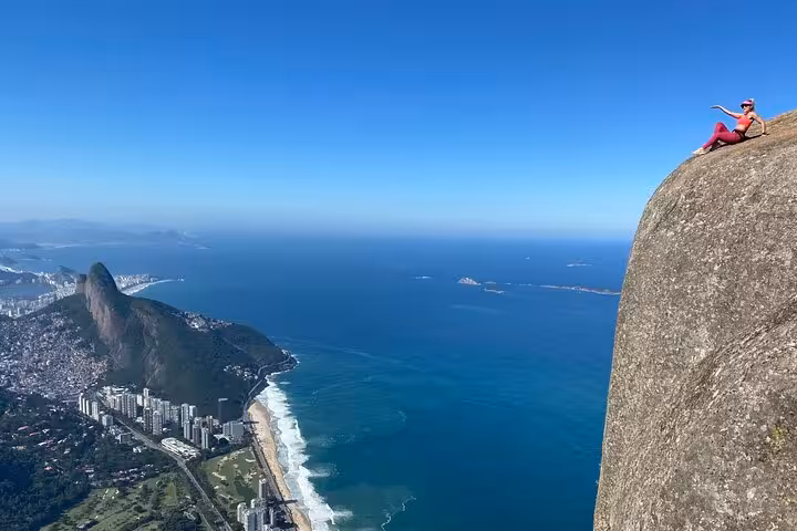A hiker sits triumphantly at the edge of Pedra da Gávea, enjoying panoramic views of Rio de Janeiro.