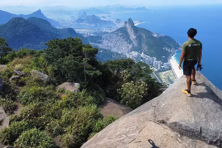 Hiker enjoys breathtaking view from Pedra da Gávea's summit, overlooking Rio de Janeiro's coastline and lush mountains.