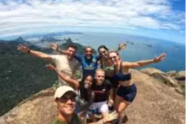 Smiling hikers reaching the summit of Pedra da Gávea with stunning ocean and forest views in Rio de Janeiro.