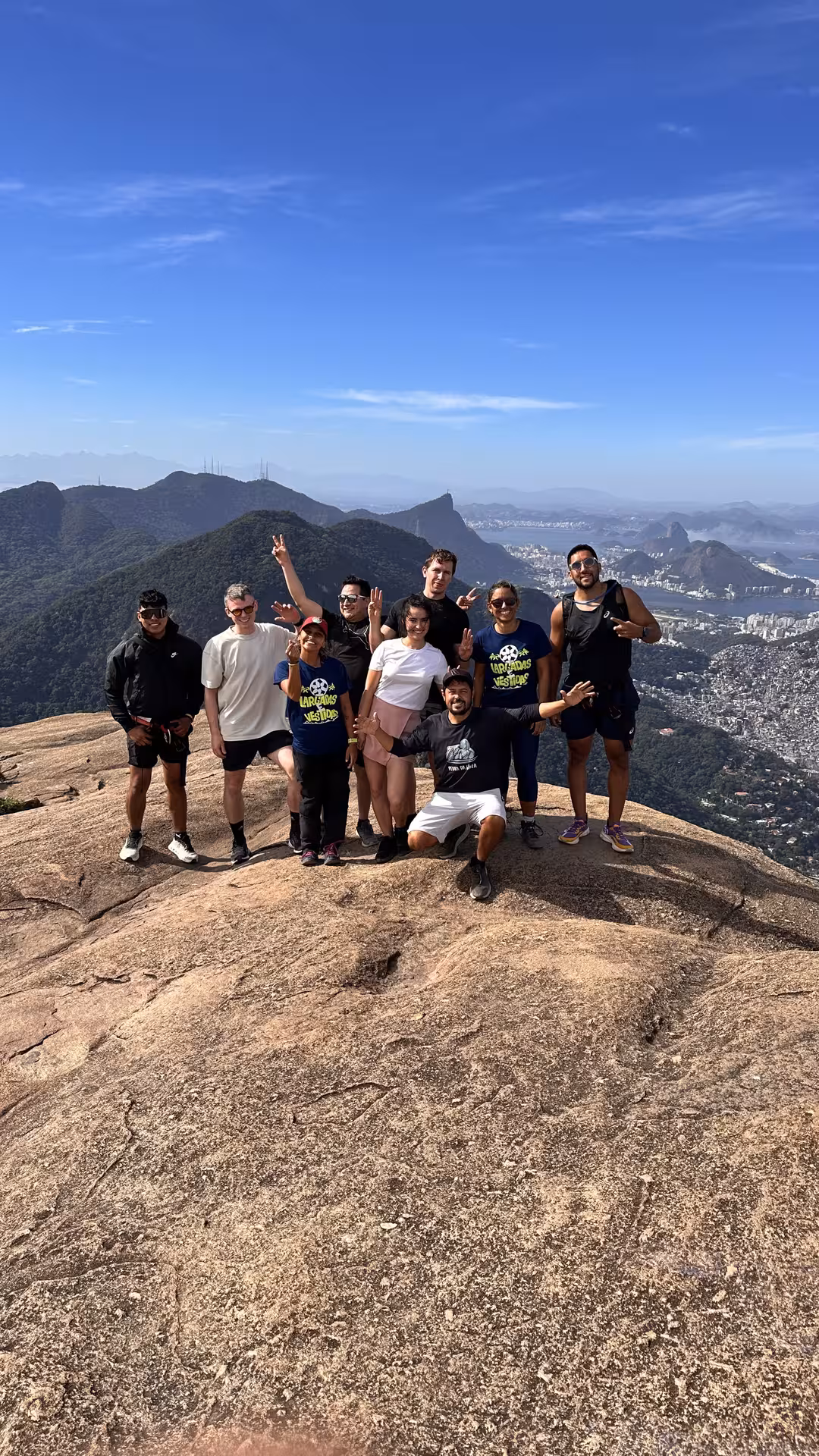 Group of hikers celebrating at the summit of Pedra da Gavea with stunning Rio de Janeiro views in the background.