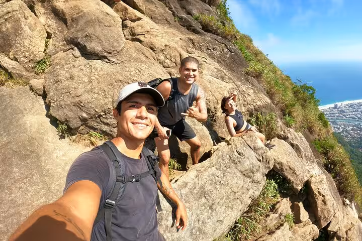 Group of hikers taking a selfie on Pedra da Gávea, capturing stunning ocean and city views in Rio.