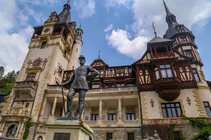 Bronze statue of King Carol I in front of Peles Castle's ornate Neo-Renaissance facade in Sinaia, Romania