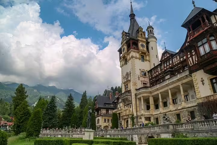 Peles Castle ornate facade with clock tower surrounded by manicured gardens and Carpathian mountains