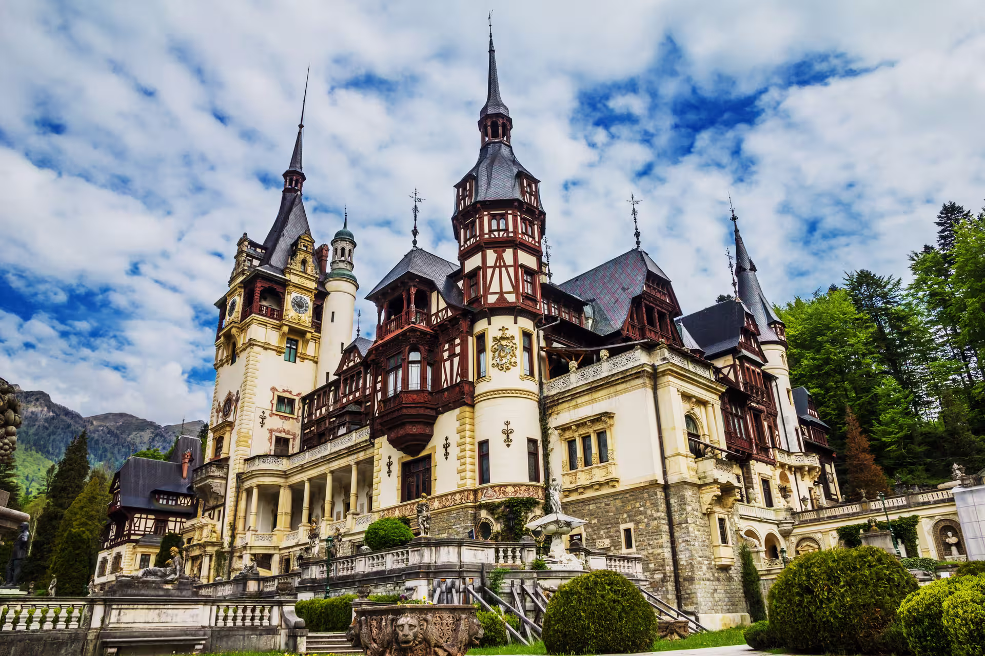 Peles Castle with its ornate towers and lush greenery set against a vibrant sky, perfect for a cultural tour in Romania.
