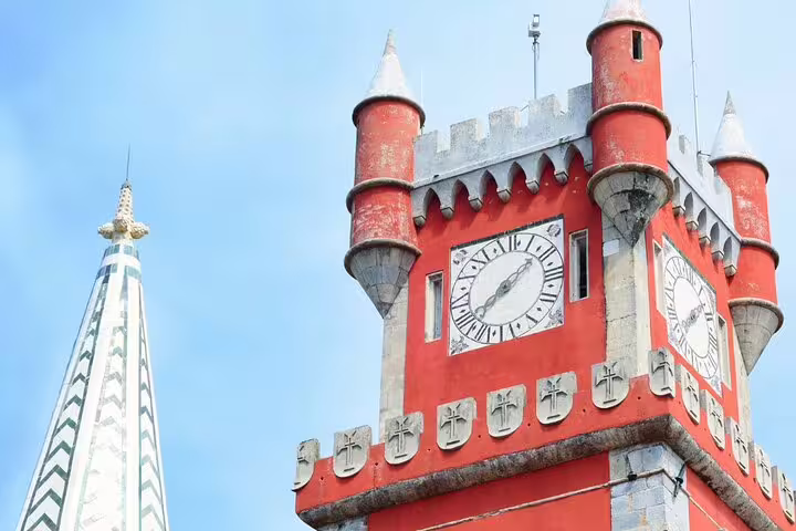 Vibrant red clock tower of Pena Palace against a clear sky, showcasing Sintra's architectural charm on a full-day tour.