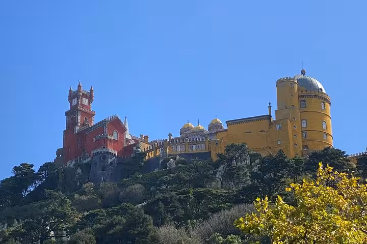 View of the colorful Pena Palace in Sintra, showcasing its vibrant red and yellow architecture against a clear blue sky.