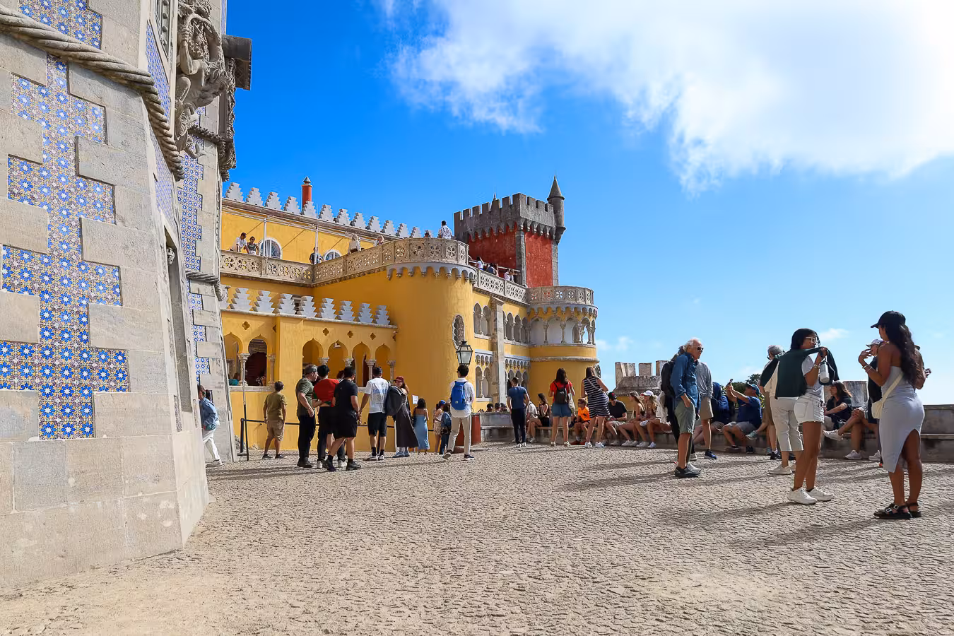 Visitors admire the vibrant architecture of Pena Palace in Sintra, with its colorful facades and intricate tile work.