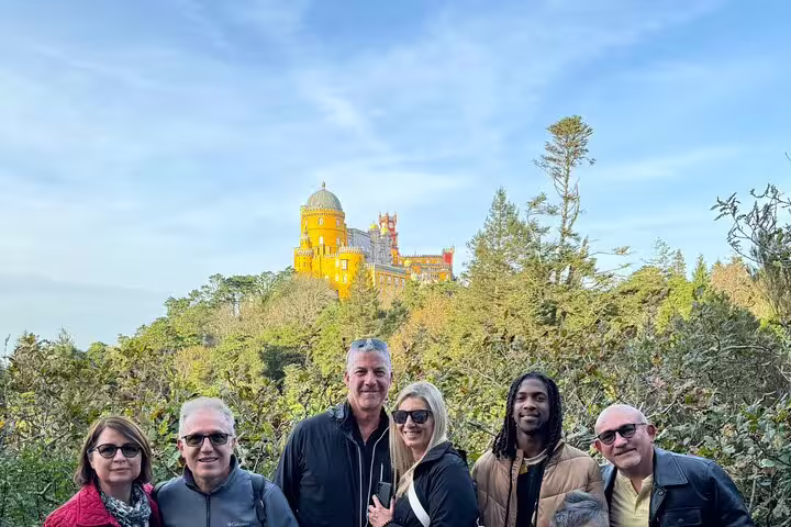 Tourists enjoying a scenic view of the colorful Pena Palace in Sintra, surrounded by lush forests during a full-day tour.