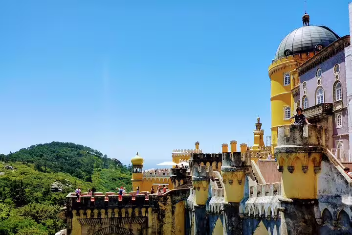 Pena Palace in Sintra under a clear blue sky, showcasing vibrant architecture and lush green hills, perfect for luxury tours.
