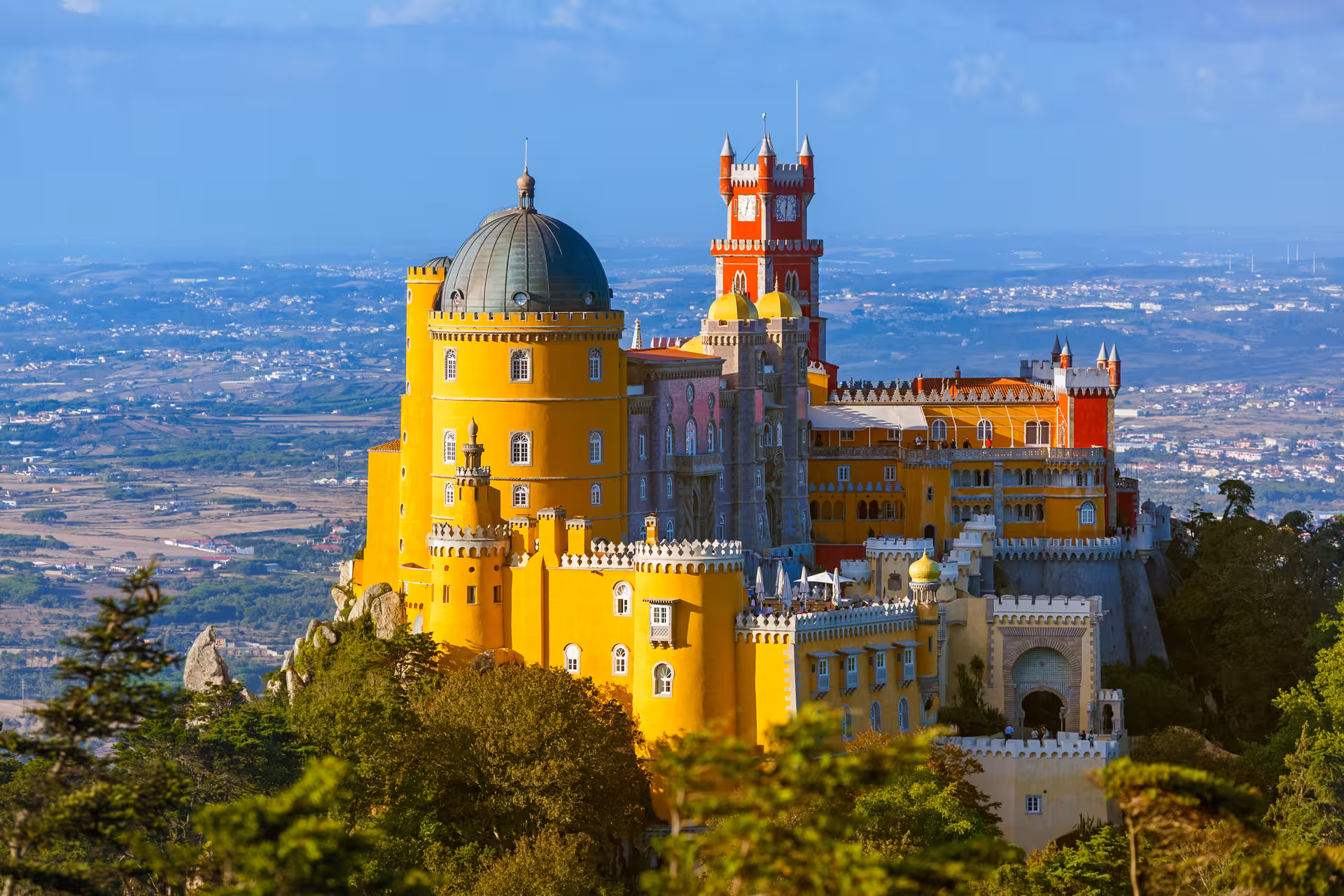 Colorful Pena Palace in Sintra, Portugal, with its vibrant yellow and red towers set against a panoramic landscape.