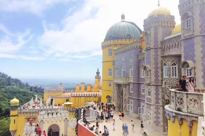 Tourists explore the vibrant, historic Pena Palace on a sunny day during a private Sintra tour, showcasing stunning architecture.