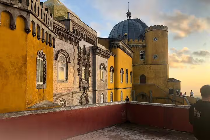 Vibrant view of Pena Palace's colorful facade at sunset, a highlight of Sintra, Cabo da Roca, Cascais day trip from Lisbon.