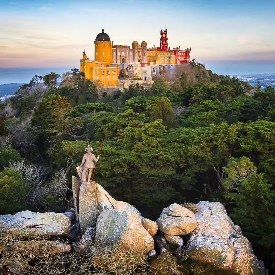 Stunning view of Pena Palace atop lush Sintra hills at sunset, featuring vibrant colors and striking architectural details.