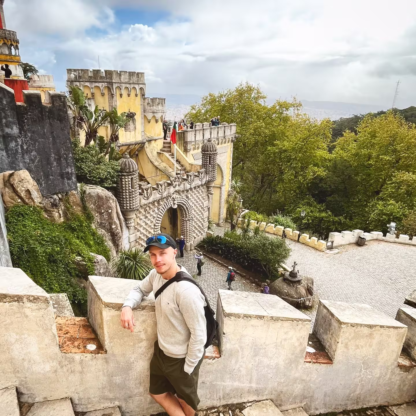 Tourist posing at the scenic stone walls of Pena Palace, Sintra, with lush greenery and intricate architecture.