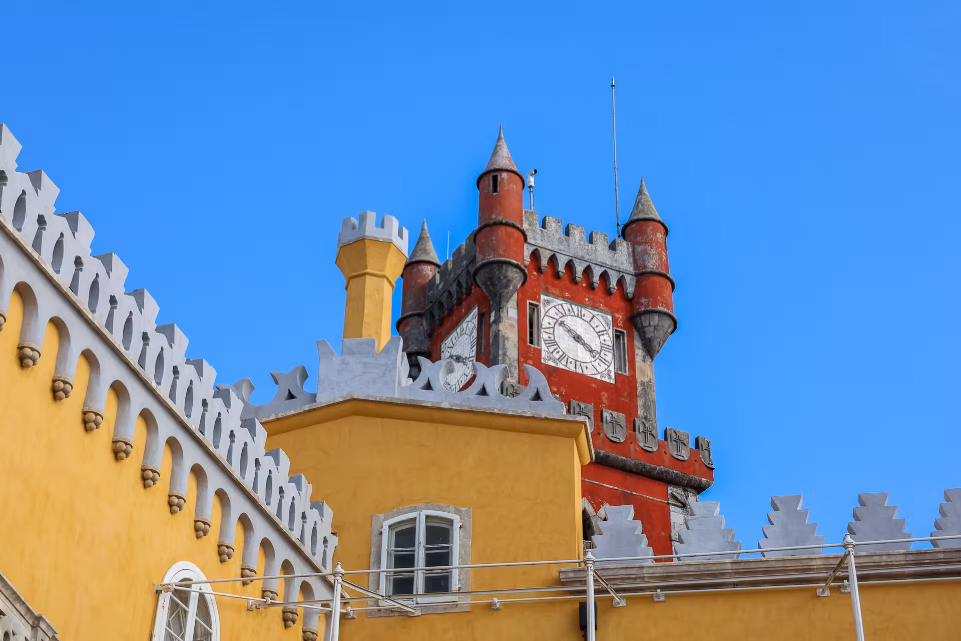 Vibrant red and yellow towers of Pena Palace in Sintra against a clear blue sky.