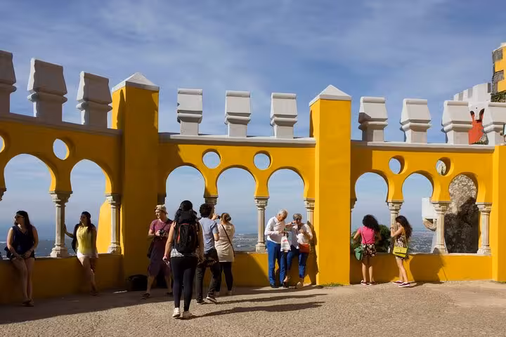 Visitors exploring the vibrant yellow walls and unique architecture of Pena Palace on a sunny Sintra Private Day Tour.
