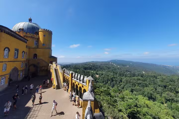 Visitors exploring the vibrant yellow facade and stunning views from Pena Palace, Sintra, on a sunny day.