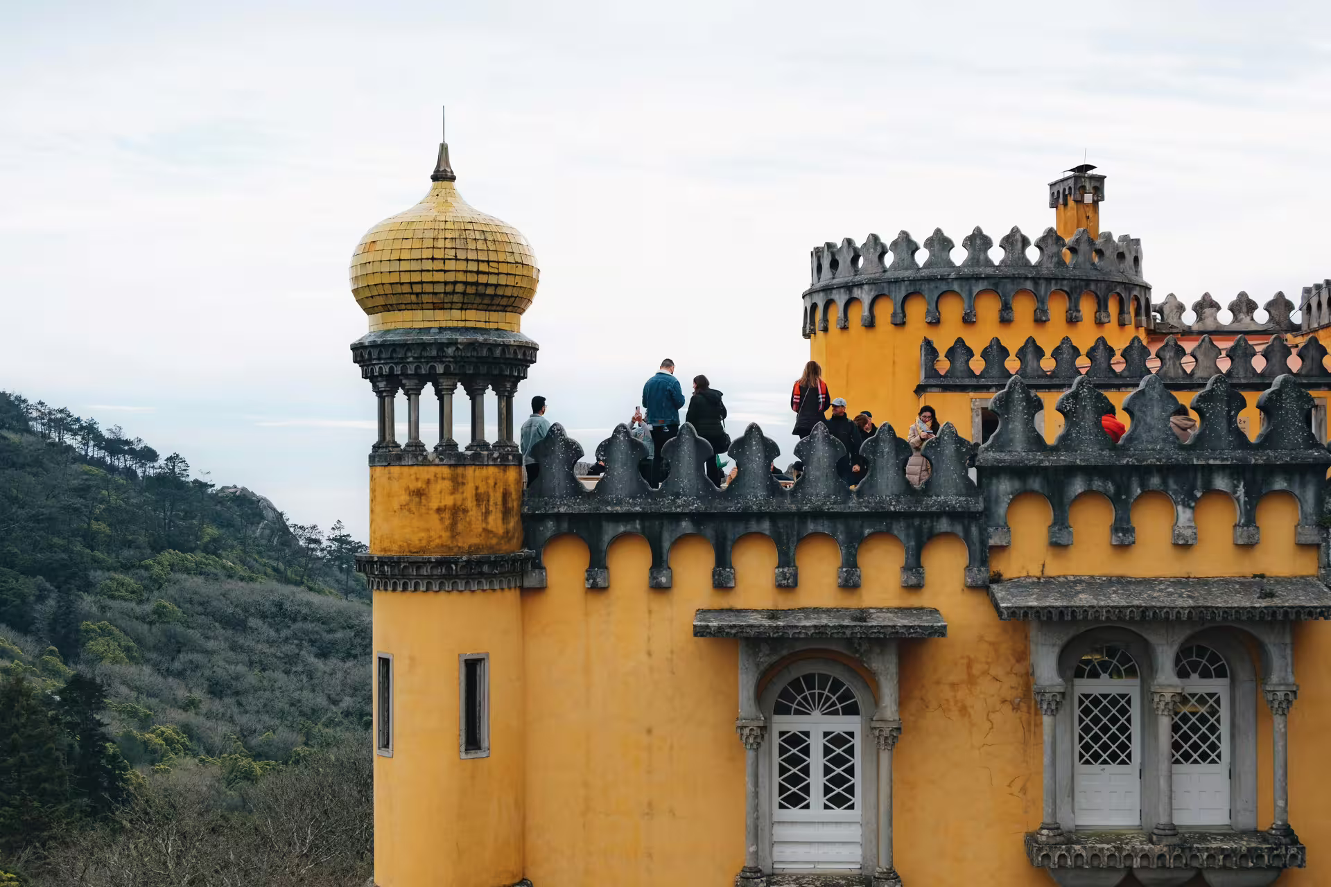 Tourists explore the vibrant yellow turrets of Pena Palace in Sintra, surrounded by lush greenery and scenic views.
