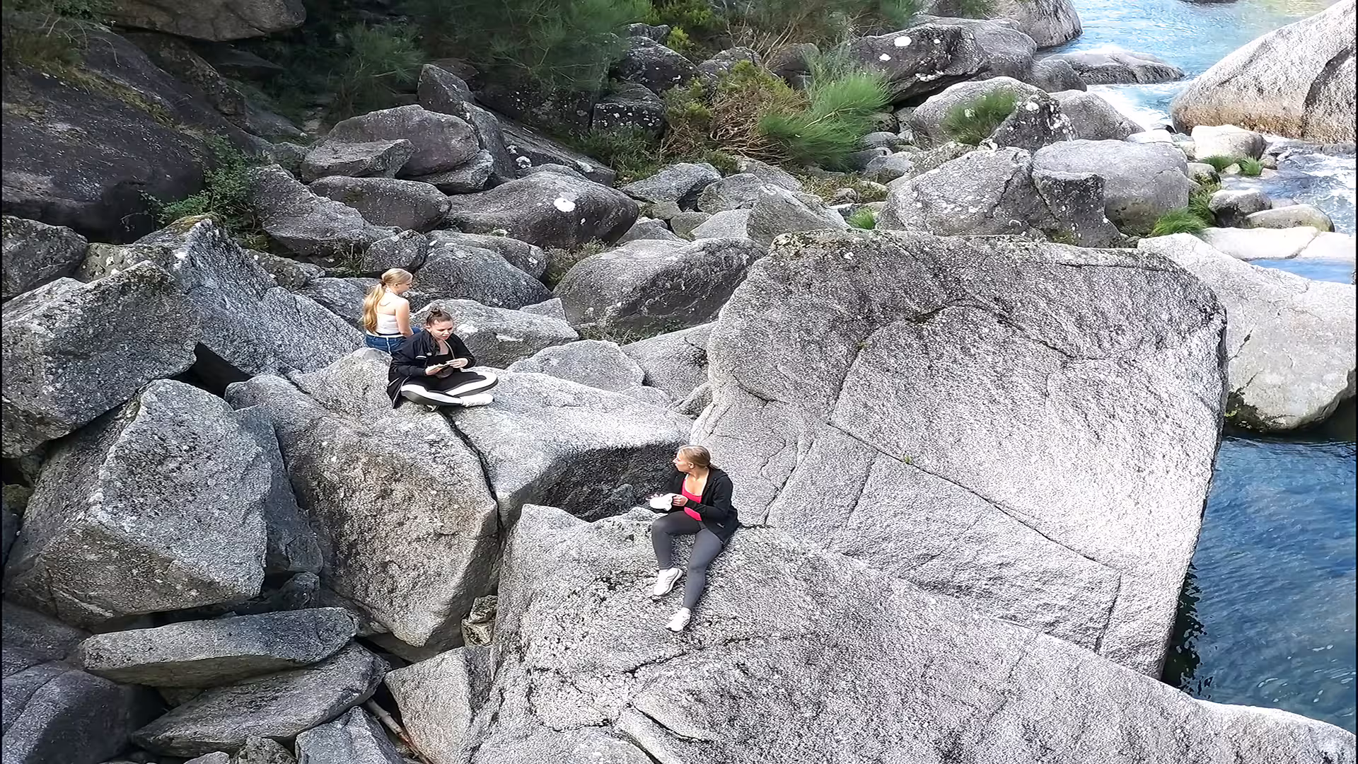 Visitors relaxing on large granite rocks by a clear stream in Peneda-Gerês National Park, perfect for nature and adventure enthusiasts.