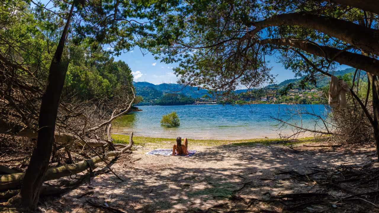Person relaxing on secluded lakeside beach surrounded by trees and mountains in Peneda Geres National Park tour.