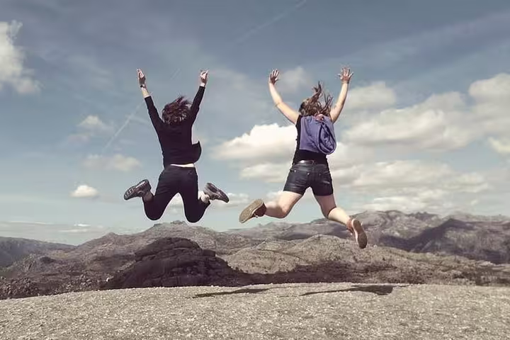 Two people joyfully leap on a rocky mountain peak in Peneda-Gerês National Park under a clear blue sky.