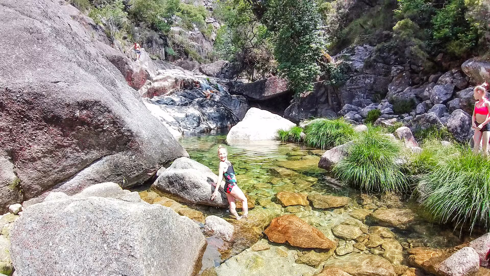 Visitors enjoying a refreshing swim in a crystal-clear natural pool surrounded by lush greenery and rocks in Peneda-Gerês National Park.