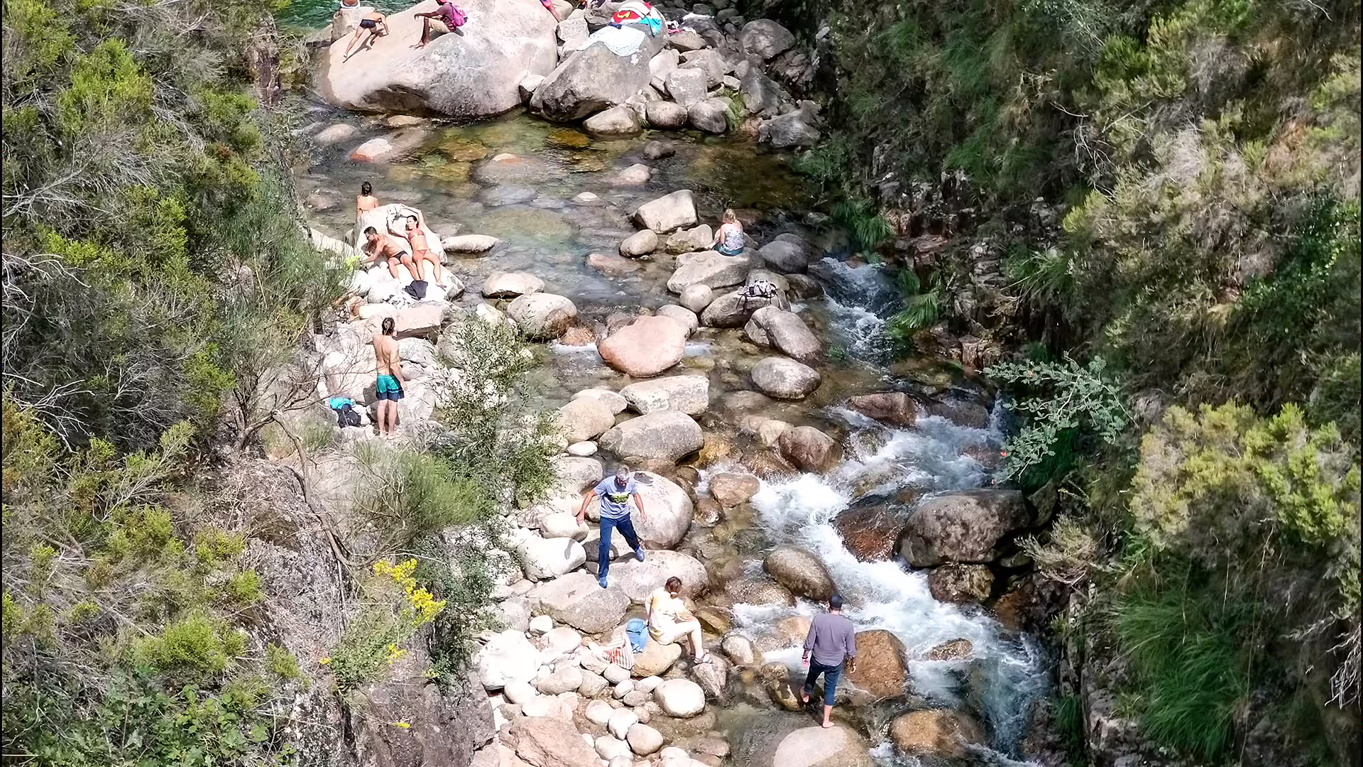 Person exploring lush greenery and rocks by a clear stream in Peneda-Gerês National Park, perfect for nature enthusiasts.