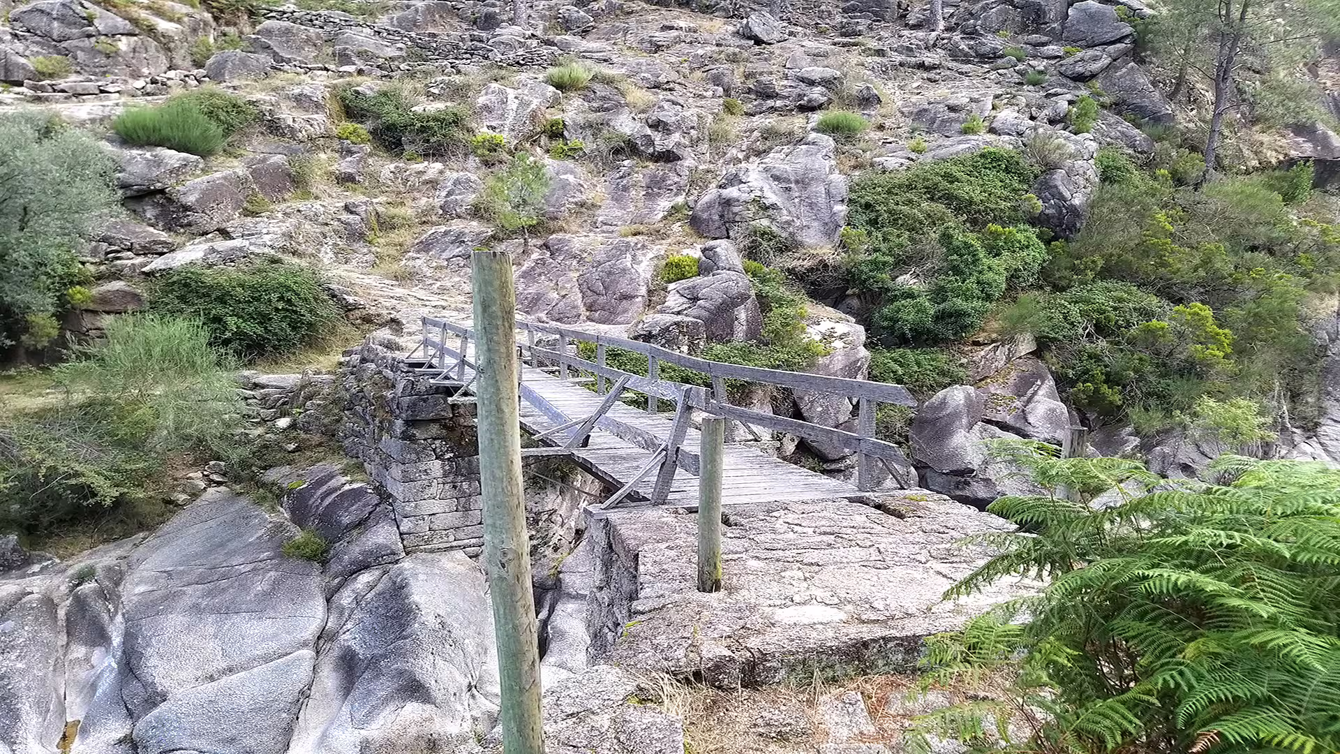 Rustic wooden bridge amidst rocky terrain and lush greenery in Peneda-Gerês National Park, perfect for nature enthusiasts.