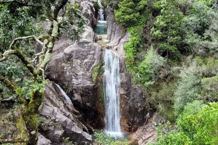 Breathtaking view of a tall waterfall surrounded by verdant forest in Peneda Geres National Park, perfect for nature tours.
