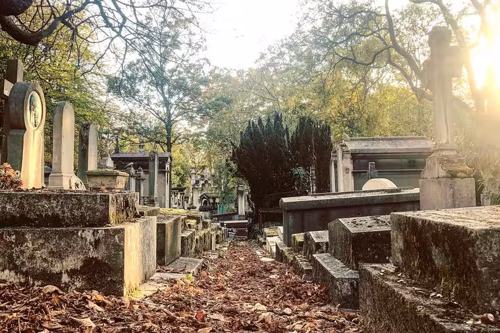 Historic stone tombs and mausoleums along a leaf-covered path at Père Lachaise Cemetery, Paris