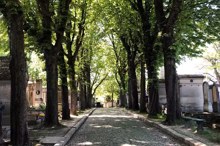 Tree-lined cobblestone path through Pere Lachaise Cemetery with historic mausoleums in Paris
