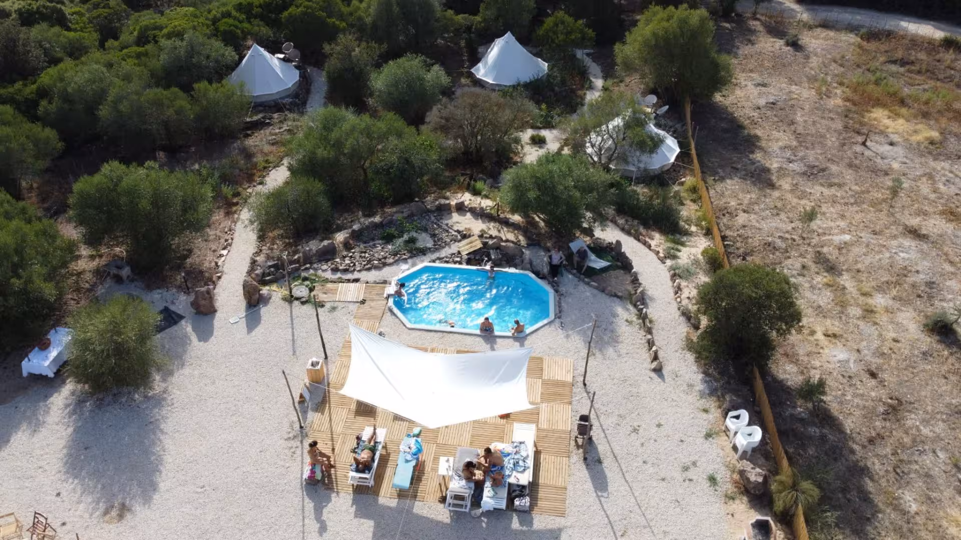 Aerial view of Perfugas glamping site with tents, pool, and lounging area surrounded by lush greenery for a nature retreat.