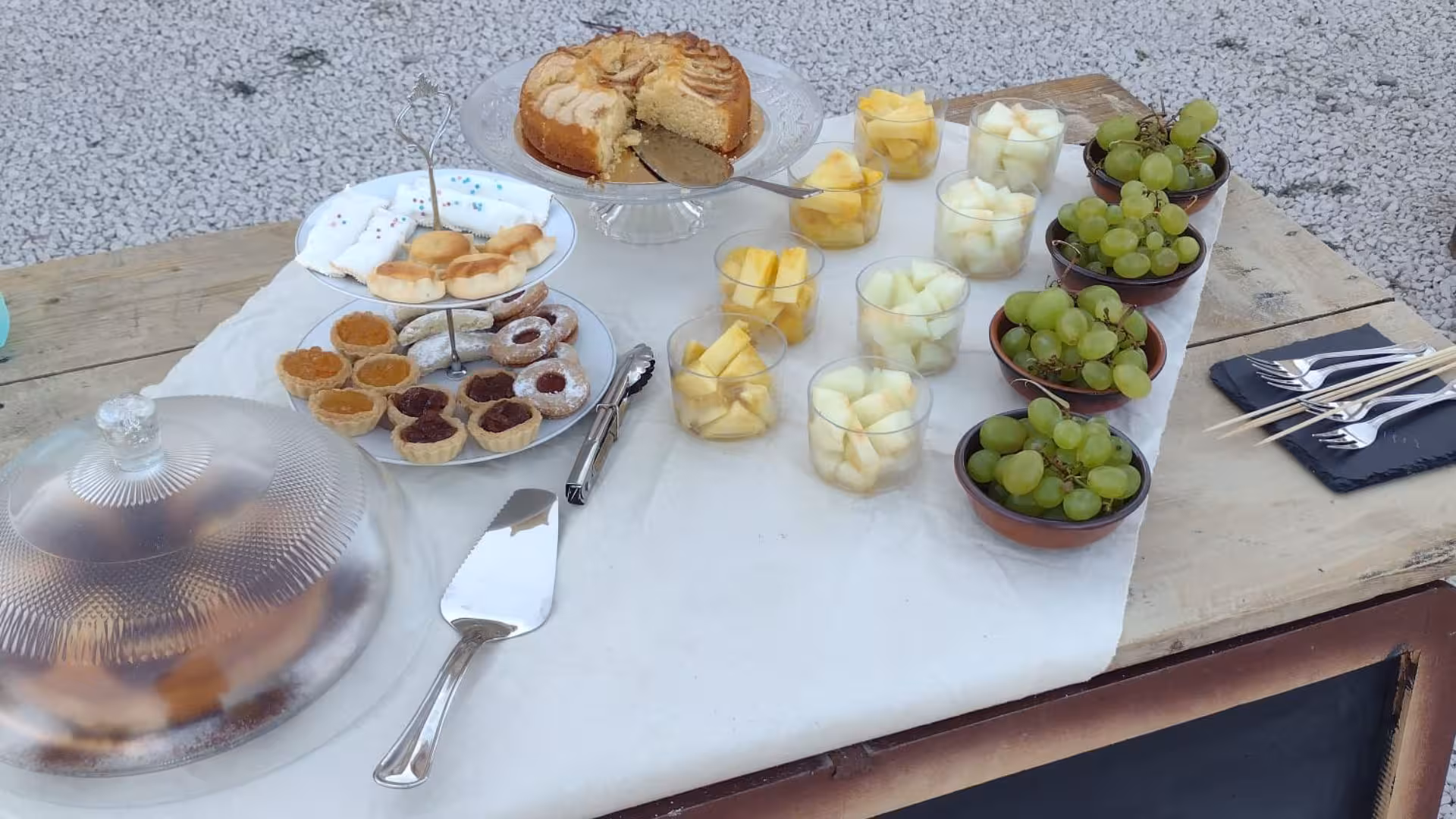 Elegant outdoor spread with fresh fruits, pastries, and a cake, perfect for a Perfugas glamping nature retreat.