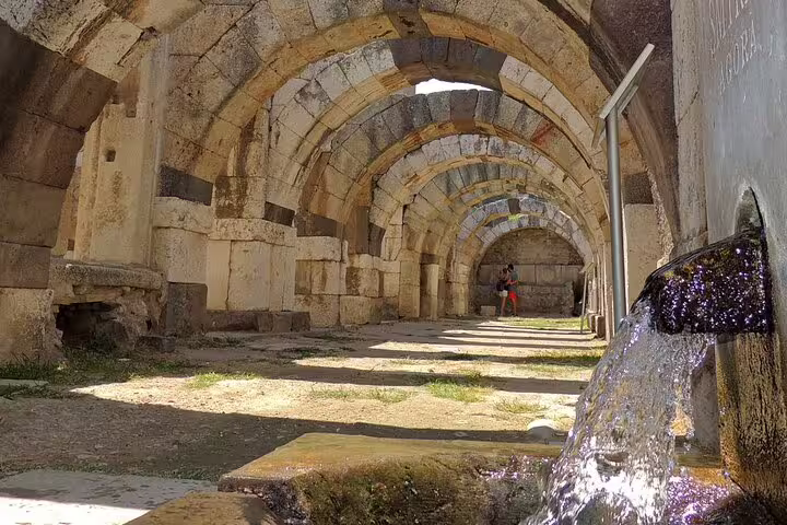 Ancient stone aqueduct arches with flowing spring water in Pergamum, highlight of 4-day mini group Turkey tour