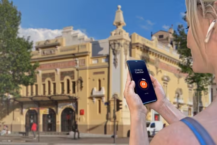 Tourist holding smartphone with GPS audio guide app in front of historic building in Perpignan