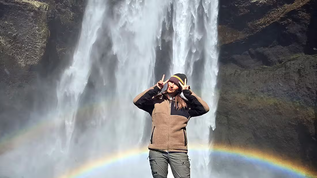 A lone person posing for a photograph in front of a large waterfall in the background
