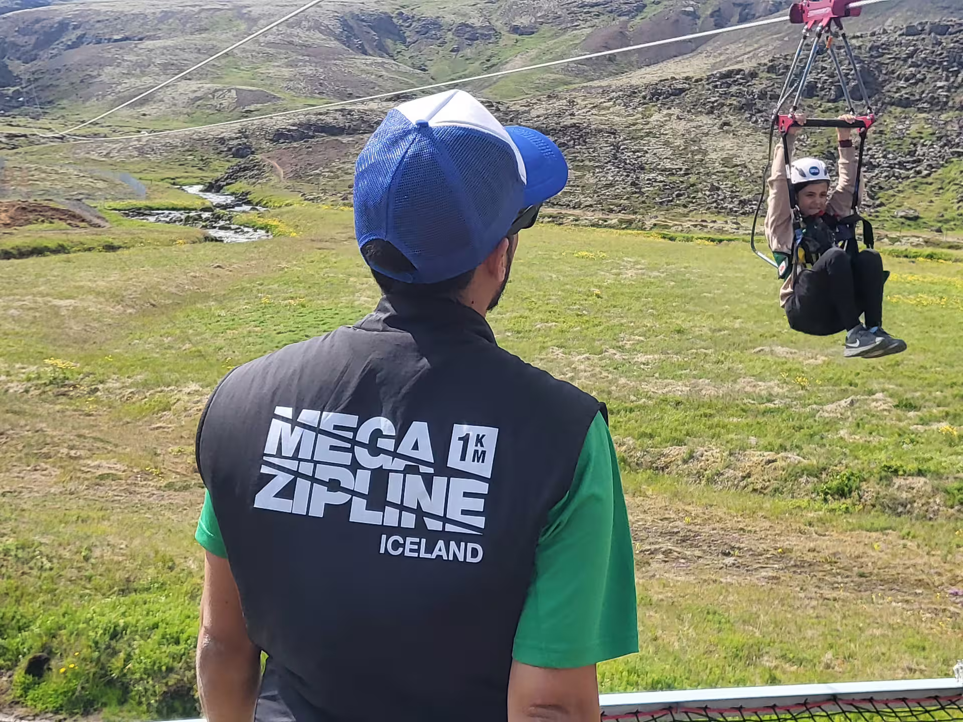 Person ziplining over scenic Icelandic landscape with guide from Mega Zipline Iceland, showcasing adventure and thrill.
