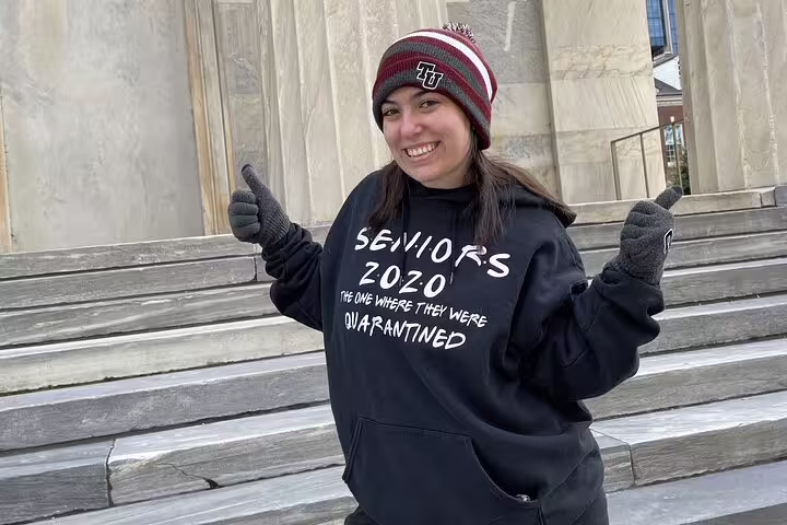 Smiling student in Seniors 2020 quarantine sweatshirt and beanie giving thumbs up on Philadelphia historic steps