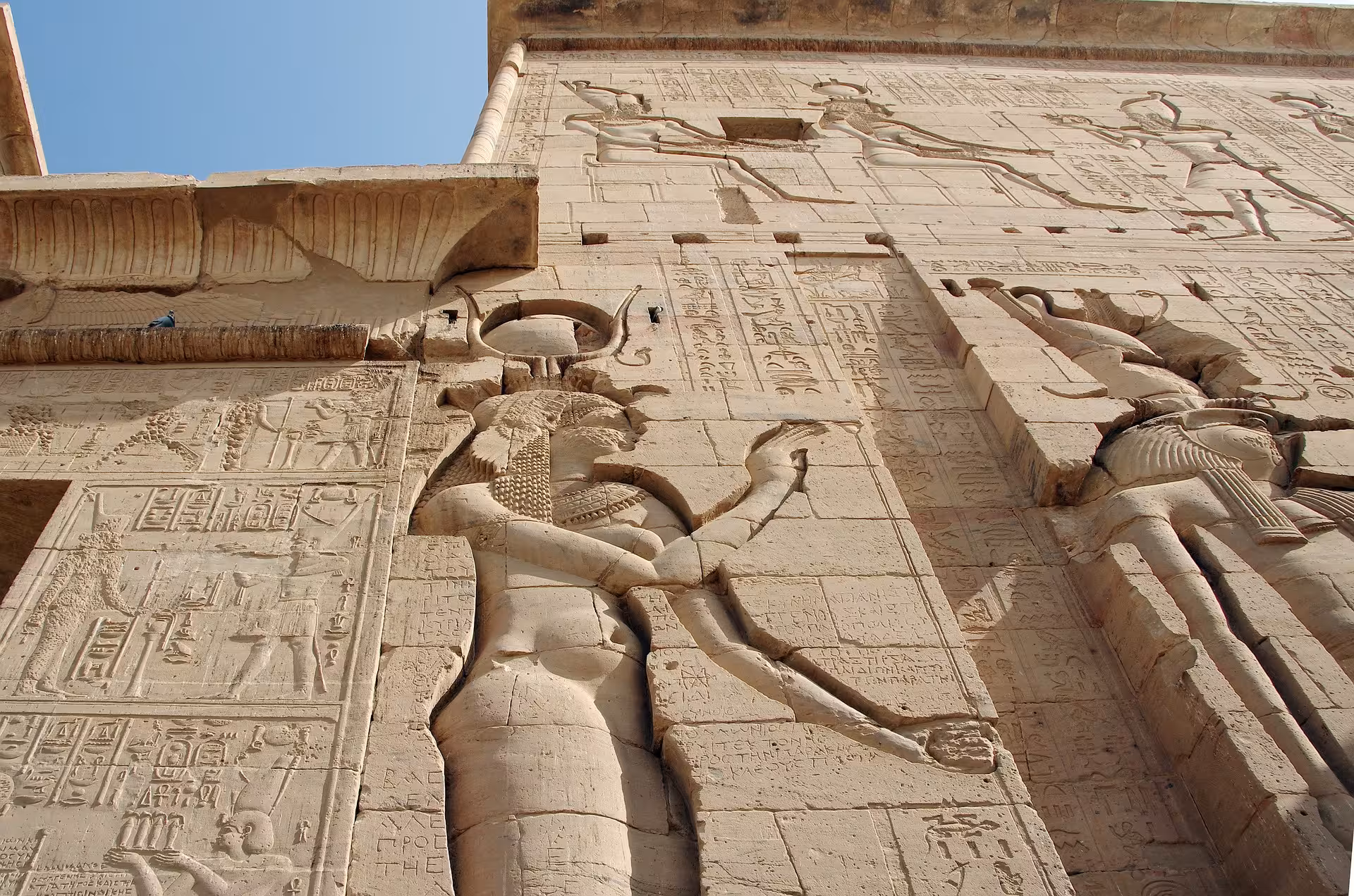 Ancient Egyptian hieroglyphic carvings and goddess relief sculptures on the stone walls of Philae Temple in Aswan