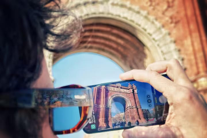 Person captures a historic archway with their phone during a photography class in a scenic park and old town setting.
