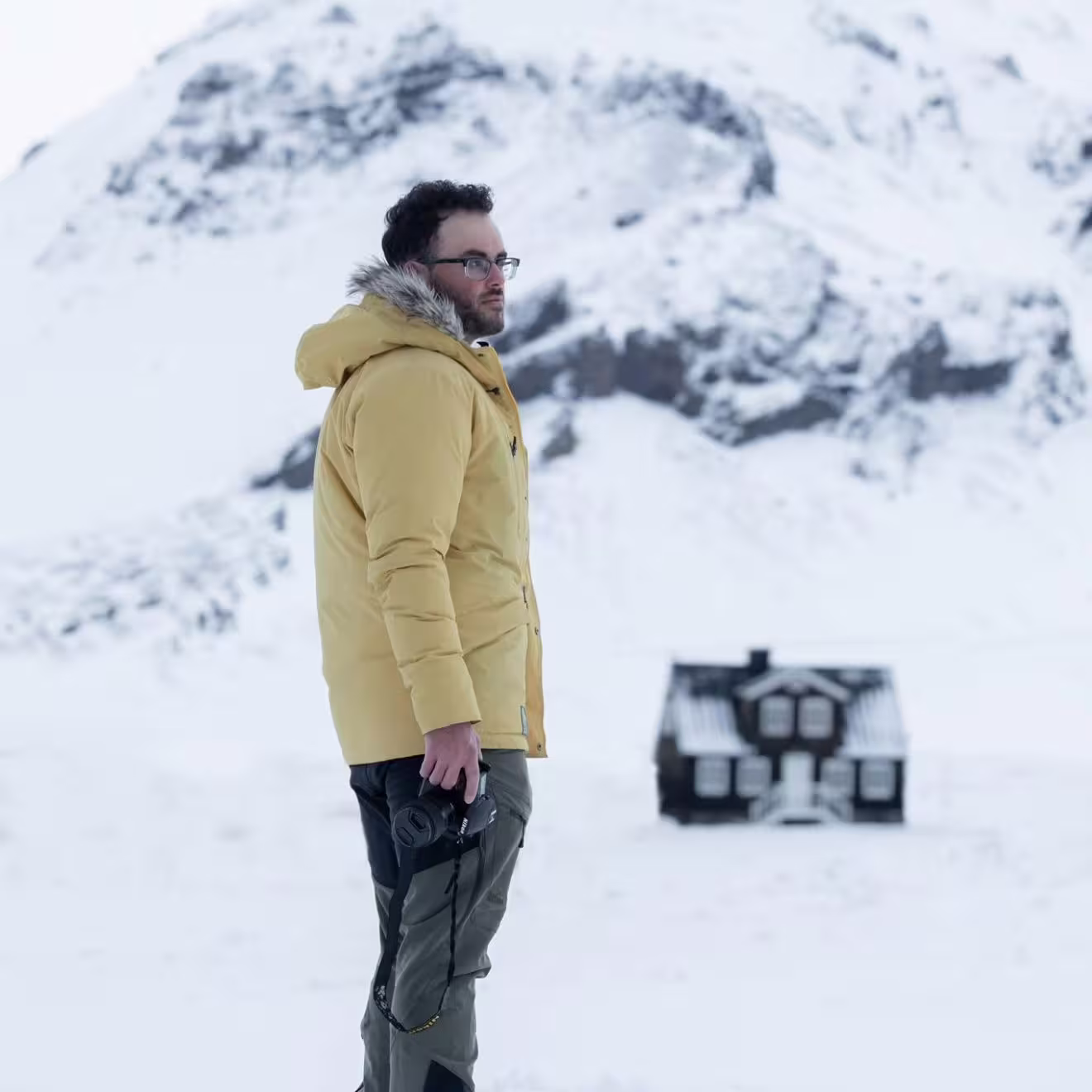 Photographer with camera standing in snowy Snaefellsnes wilderness with isolated Iceland cottage and mountain behind