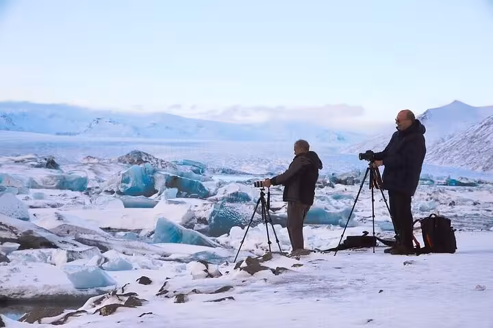 Two photographers with tripods capturing icebergs on Iceland's snowy south coast glacier lagoon