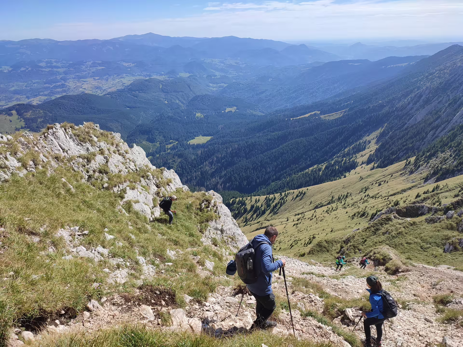 Hikers ascending steep rocky trail on Piatra Craiului ridge with panoramic mountain valley views from Brasov