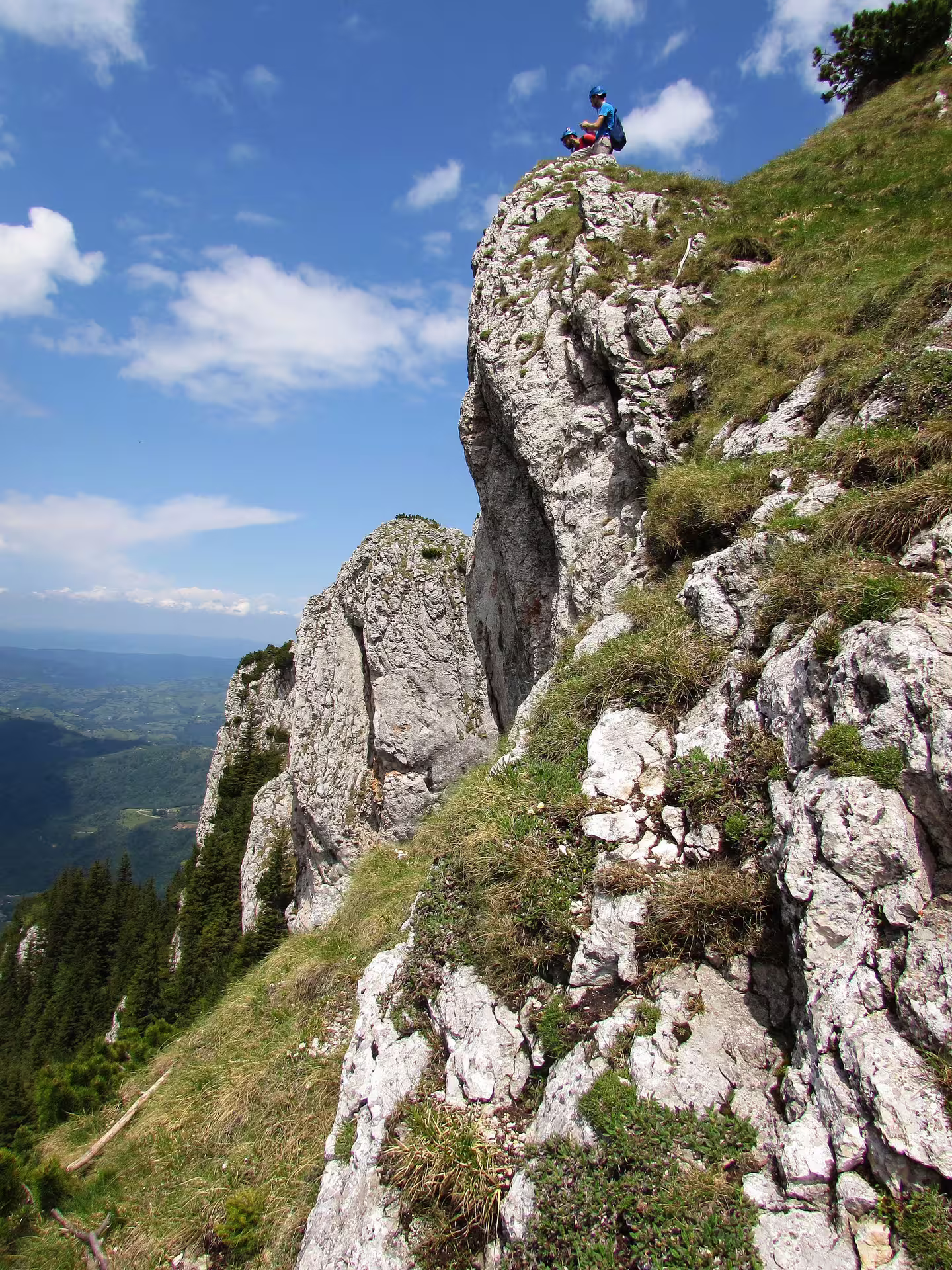 Hikers resting on rocky limestone ridge of Piatra Craiului with panoramic valley views below