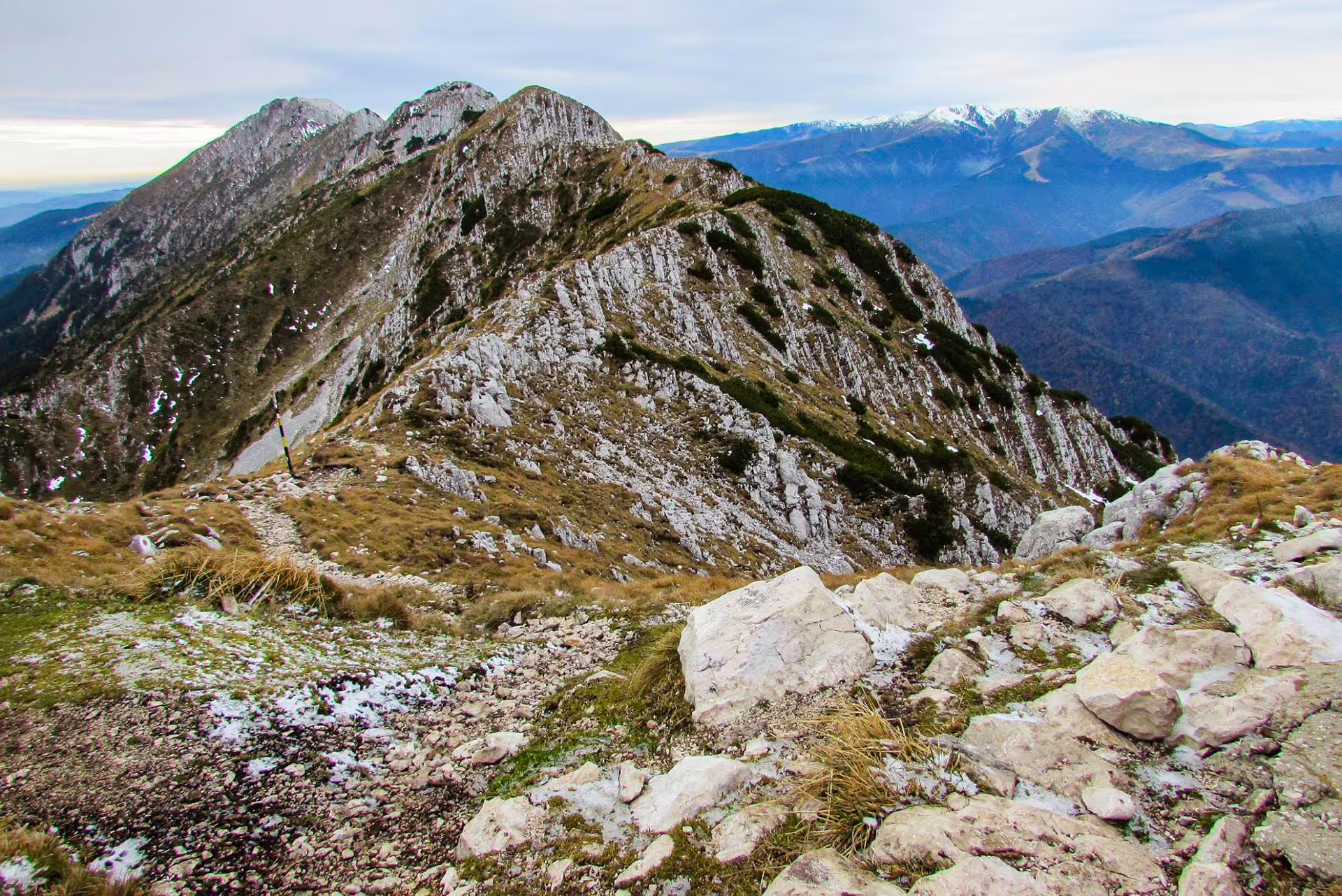 Rocky ridge trail on Piatra Craiului mountain with limestone cliffs and snow-capped peaks in background