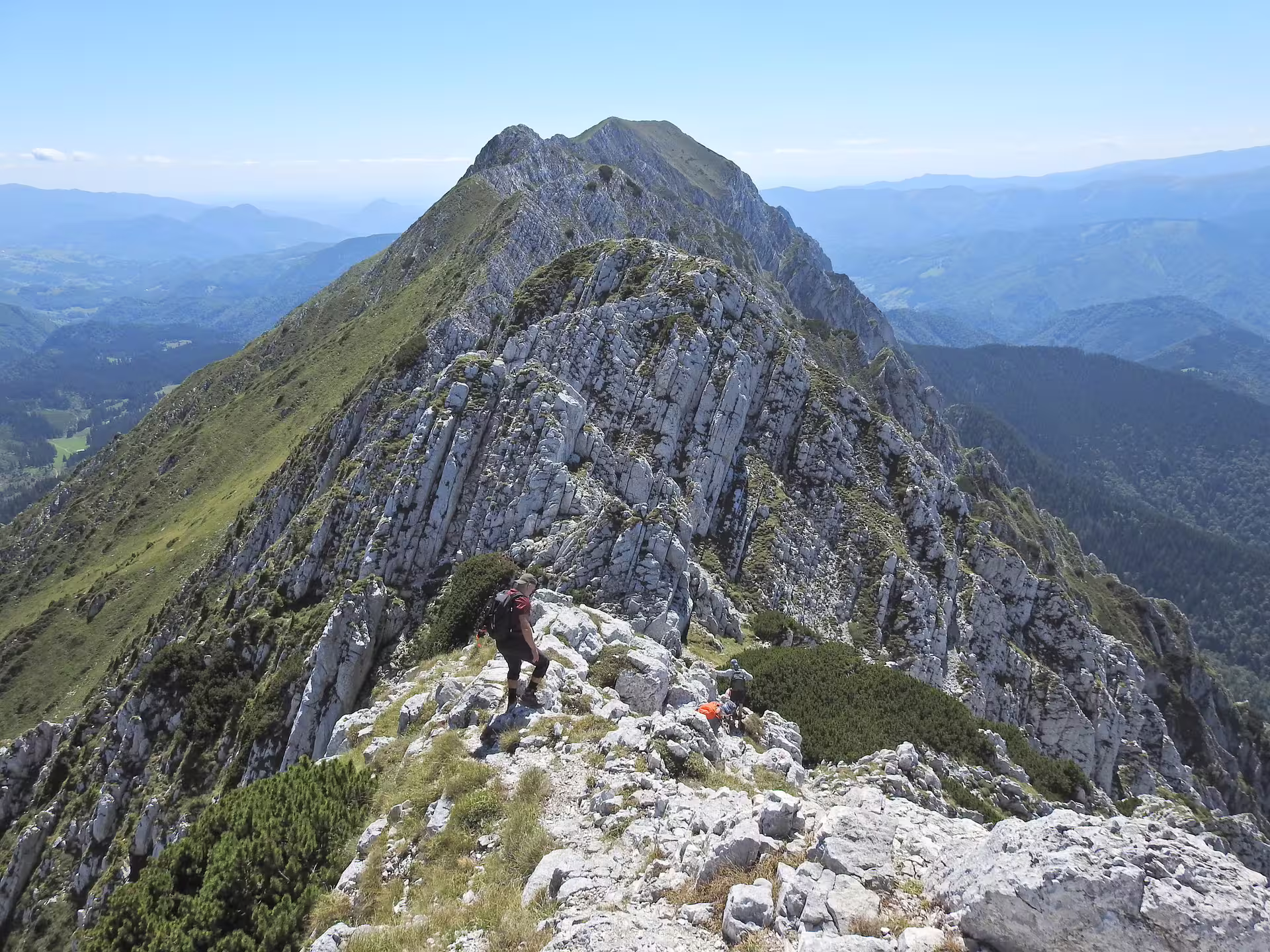 Hikers traversing a rocky ridge on Piatra Craiului mountain with panoramic views of Brasov valleys