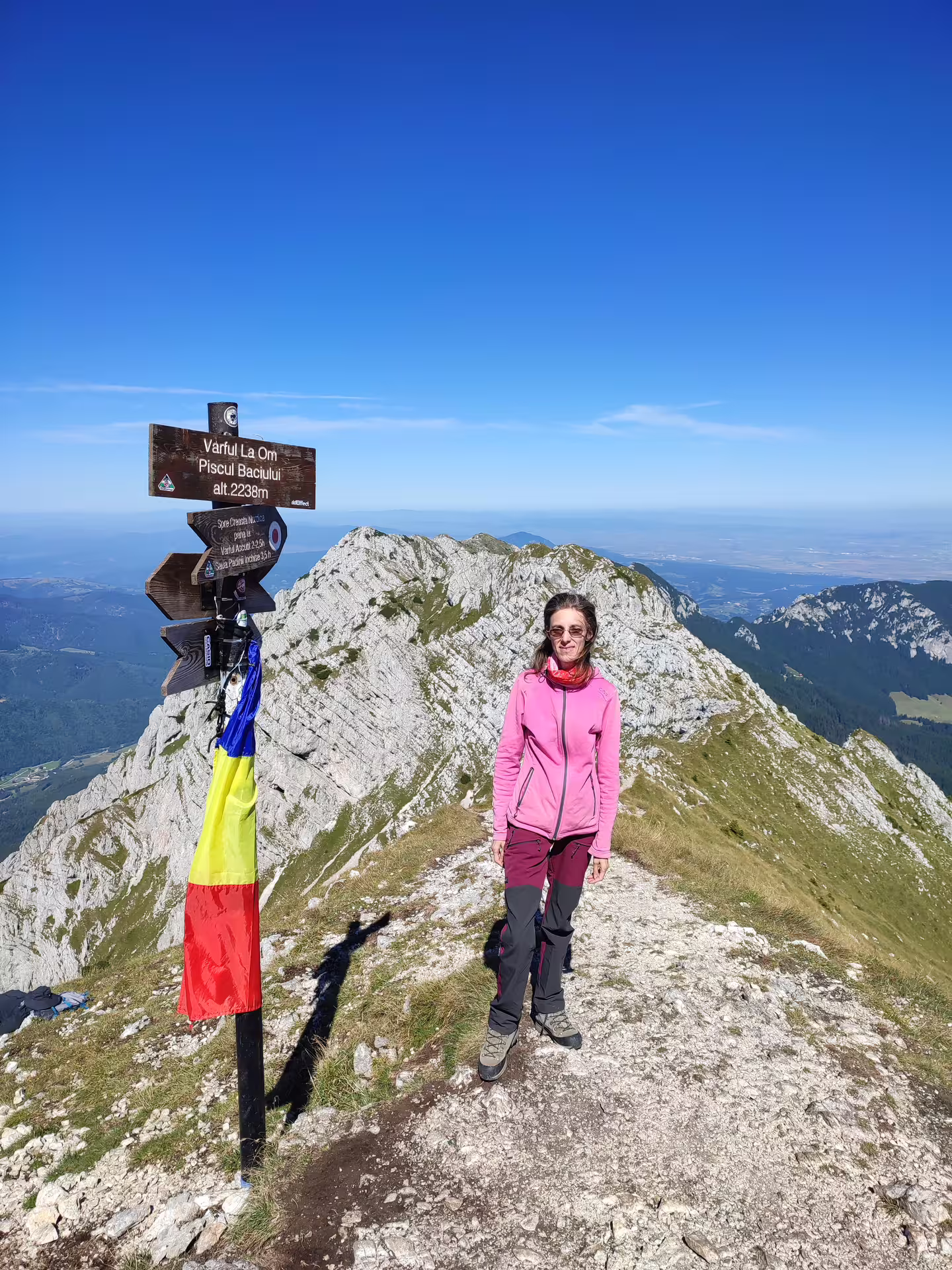 Hiker at Vârful La Om summit sign, 2238m, Piatra Craiului mountains, Romania, clear blue sky